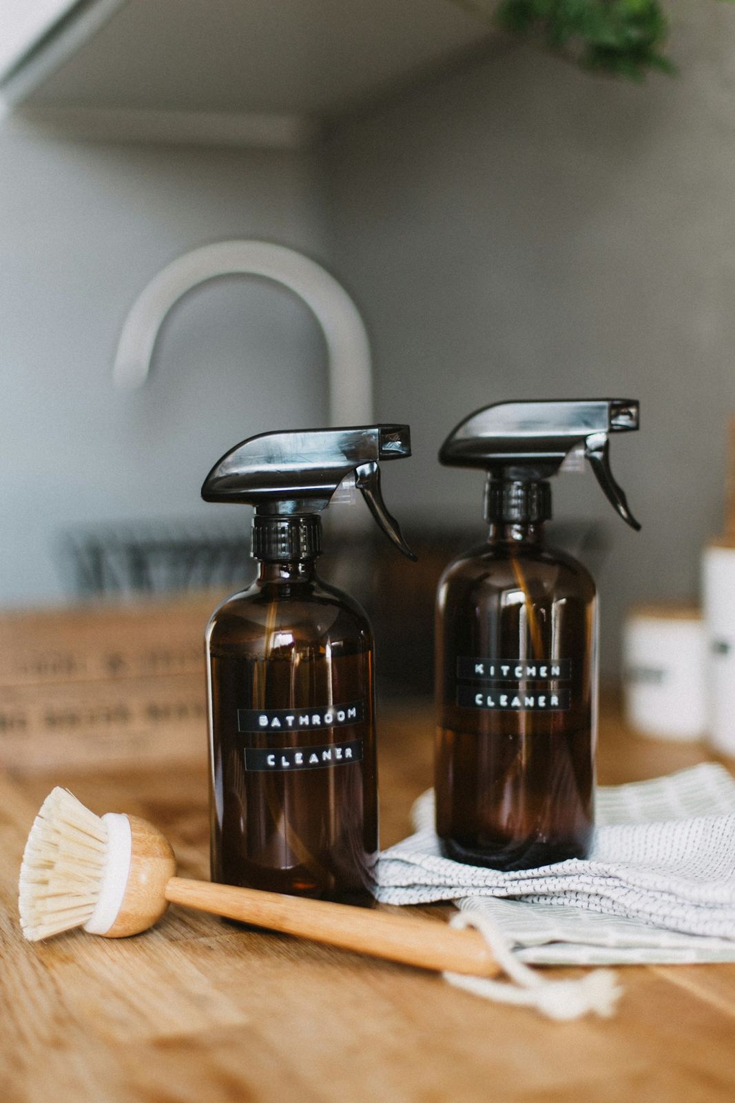 Amber spray bottles of cleaner with a wooden scrub brush