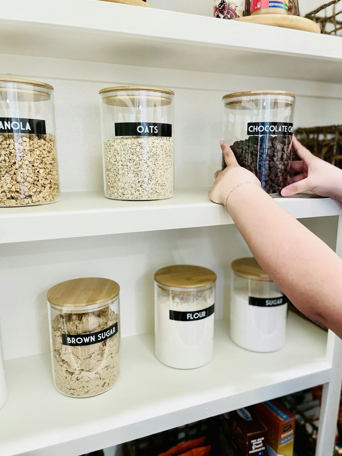 Glass jars of oats, rice and dry goods on white pantry shelves