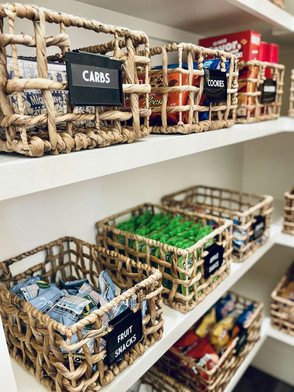 Woven baskets of snacks and pantry staples neatly labeled on white shelves